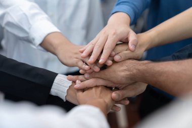 Çeşitli ofis çalışanlarından oluşan bir grup, ofis odasında el ele vererek iş sinerjisini ve iş yerindeki güçlü verimli takım çalışmasını sembolize ediyor. İş çalışanları arasındaki işbirliği ve birlik. Tedbirli