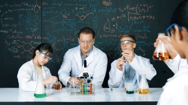 Zeki öğretmen, öğrenci renkli çözeltileri karıştırırken ya da deney yaparken kimyasal teoriyi açıklar. BTMM fen dersinde karatahtaya işaret ederken, eğitmen kimya öğretiyor. Öğretim.