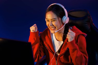Yüzünde kulaklık renginde kulaklık takan, neon odada online oyun oynayan, Esport meziyetli takım oyuncularına yumruk kaldırarak oynayan güzel Asyalı kız flamasının sunucu kanalı. Taktik.
