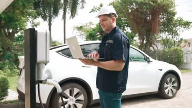 Evde EV şarj istasyonu kurulumu üzerinde çalışan nitelikli teknisyen, EV için dizüstü bilgisayarla şarj sisteminde sorun çıkarma ve yapılandırma ayarları yapıyor. Titiz