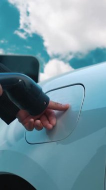 Elektrikli araç, iş adamı yüksek gökdelenlerle çevrili kentsel alandaki şarj istasyonunda EV akü şarj ediyor. Çevre dostu yenilikçi temiz enerji kavramı.