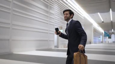 Mutlu iş adamı beyaz koridorda yürürken başarılı projesini kutluyor. Yatırımcı, terfi almak ya da satışları artırmak için telefon kullanarak iyi haberler alıyor. Mutluluk, neşe. Sevinçli..