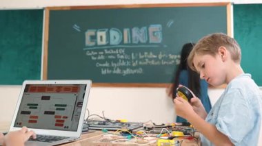 Kafkas arkadaşı STEM sınıfında elektrik panosunu tamir ederken Asyalı çocuk kodlama programı. Enerjik öğrenci kodlama mühendisliği komut yazarken ve yapay zeka yazılımını programlarken tahtada duruyor. Pedagoji.