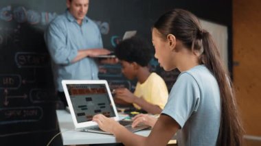 Afrikalı erkek manken tamir ederken beyaz kız programlama ya da kodlama sistemi. Öğretmen elinde dizüstü bilgisayar tutarken çeşitli çocukların web geliştirme programı yazmalarına bakıyor. Yenilik eğitimi. Öğretim