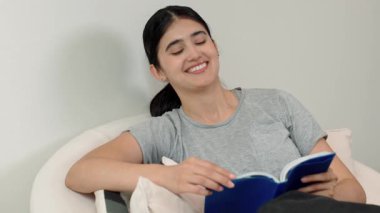 Kanepede oturan bir kadın ders kitabı okuyarak sosyal ve mesleki teknoloji bilgisini artırır ya da akıllı bir anne olmak için çocuk yetiştirir. Hayat boyu öğrenme konsepti. Uyumsuzluk.