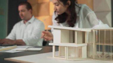 Bir grup mimar mühendis birlikte çalışıyor ve ofis tasarımı hakkında tartışıyorlar. Genç mühendis ev modelini ölçerken yönetici dizüstü bilgisayar kullanıyor. İş tasarımı konsepti. Yönlendirici.