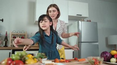 Zeki beyaz anne ve Asyalı kız birlikte yemek pişiriyor ve sebze doğruyor ya da akşam yemeği için salata hazırlıyor. Mutlu anne ve kız taze yemekle sağlıklı yemek yapıyorlar. Sağlıklı gıda konsepti. Pedagoji.
