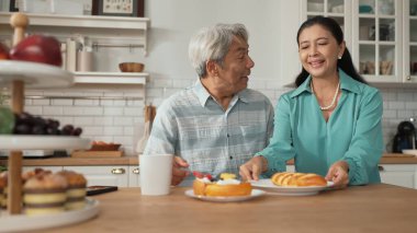 Büyükannem kahvaltısını sunarken, gülümseyen büyükbaba masada oturuyor. Yaşlı çift konuşuyor ve birlikte vakit geçiriyorlar ya da birlikte destek oluyorlar. Sağlıklı ilişki kavramı. Myrmidon.