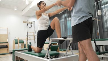 Esneklik ve çekirdek eğitimi için pilates kursunda trapez masasında destek alan bir kadın. Öğrenci dengeyi geliştirmek için reformcuları iki büklüm ediyor. Alışkanlık.