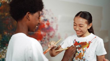 Resim dersinde, renkli duvarda, boyalı beyaz gömlekleri boyayarak gülümseyen farklı çocuklar. Tecrübe alışverişini temsil etmek, birbirimizi öğrenmek. Öğretim.