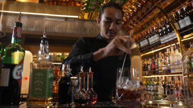Zeki Asyalı barmen bardakta karıştırılmış alkol şurubunu buzla karıştırıyor. Çünkü kayanın üzerinde kamera var. Gece kulübünde taze kokteyl kokteylleri karıştırıyor. Vinosity.