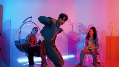 Çok kültürlü bir arkadaş kürsüde otururken Asyalı yetenekli bir dansçı modern müziğe geçiyor. Profesyonel dansçı, hipster takımı tezahürat yaparken ve desteklerken enerjik adımlar atıyor. Mutluluk.