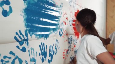 Küçük çocukların el kaplamalarını renkli ve boyalı duvarlarla çiziyorlar. Sanat dersinde kırmızı ve maviyle boyanmış boya odasıyla karışık ırk tutma tepsisiyle lise öğrencisi. Yaratıcı aktivite. Öğretim