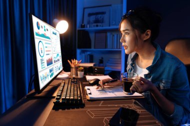 Elinde kahve fincanıyla bilgisayara bakan Asyalı güzel yaratıcı bir kadının iş piyasası grafik klasörü raporuna gece vakti işaret ettiğini düşünmek. Taktik.