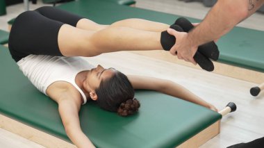 Pilates müşterisi pilates minderinde yuvarlanırken bacak kaldırma alıştırması yapıyor. Kadın, karın bölgesini güçlendirmek ve esnekliği artırmak için antrenörlük yaparken ters duruşta poz veriyor. Alışkanlık.