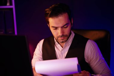 Stresli akıllı işadamı, gece geç saatlerde Mor Neon Koyu Işık Odası 'ndaki disiplin ürünleri servisinin çevrimiçi satış kanalını oluşturmak için kağıt işi raporu klasöründeki pazar verilerini analiz ediyor. Tahmin et..