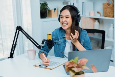 Sosyal medyada kulaklıkla canlı yayın yapan Asyalı sunucu modern stüdyoda yaşam koçluğu veya pazarlama dinleyicilerini selamlıyor. Taktik.