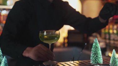 Midori Ekşi Kokteyli 'nde karamelize edilmiş turunçgil dilimi ve tarçın gücüyle barmen lüks Noel ağacı temalı bir barda akıllı bir konuğa ikram ederek şık bir fincan çay kadehi servis etti. Vinosity.