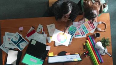 Akıllı tasarımcının renkli paletlerden renk seçmesine yardım ederken yukarıdan aşağı görünümü. Dizüstü bilgisayardan logoya bakarken birlikte çalışan ve planlayan iş adamlarının hava görüntüsü. Sempozyum.