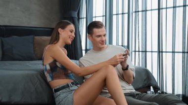 Genç çift, kredi kartıyla ödemek için internet üzerinden ödeme uygulaması ve dijital cüzdan kullanarak yatak odasında oturuyor. Mobil internet üzerinden alışveriş ve modern alımlar. Düzenle