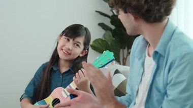 Akıllı kız oturma odasında ukulele çalarken beyaz bir babanın motivasyona ve teşviğe el çırpması. Amerikalı kız babasına gösterirken gitar öğreniyor. Aile yaratma kavramı. Pedagoji..