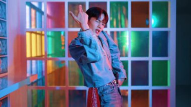 Kameraya bakarken kollarını esneten seksi kıyafetli Asyalı dansçı. Profesyonel sanatçı gece kulübünde renkli neon ışıkları canlı bir şekilde dururken serbest stil dansı yapıyor. Mutluluk.