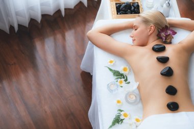 Lüks tatil beldesindeki kaplıca salonunda sıcak taş masajı. Gündüz huzurlu ortam, mutlu kadın müşteri bazalt taşı masajının keyfini çıkarıyor. Sessiz.