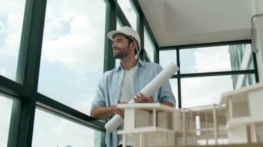 Gökdelen manzarasına bakarken yürüyen profesyonel mimar mühendisi. Masaya yerleştirilmiş ev modeliyle pencereye bakarken yetenekli proje yöneticisi proje planını tutuyor. Tasarım. İzleme