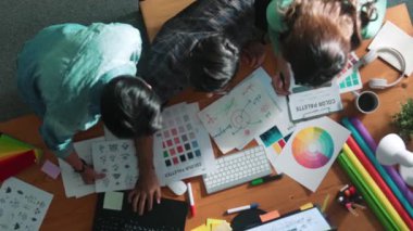 Tasarımcı fikirleri yazarken proje yöneticisinin yukarıdan aşağıya bakan görüntüsü. Akıllı iş adamları logo tasarımı fikrini açıklarken tasarımcılar palete bakarken temayı seçiyorlar. Sempozyum.