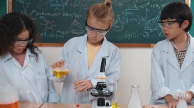 Kafkasyalı öğrenci deney yapıyor ve laboratuvarda yeni yenilikler keşfetmek için bekleyen meraklı çocuklarla çevrili biyokimyasal solüsyon döküyor. Çeşitli mutlu öğrenciler deney yapıyor. Pedagoji.