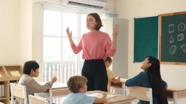 Beyazca öğretmeni, ilkokulda karatahta başında dururken vücut jesti kullanarak çok kültürlü öğrencilere teoriyi öğretiyor ve açıklıyor. Yetenekli öğretmen çocuklara soru soruyor. Pedagoji.