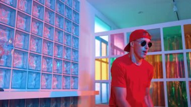 Komik break dansçı kameraya bakarken hiphop 'a doğru serbest adım atıyor. Çılgın mutlu hipster dans edip sokak dansı yaparken Led ışığında günlük kıyafet ve güneş gözlüğü takıyor. Mutluluk.