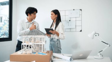 Güzel, genç, beyaz bir proje yöneticisi Asyalı mühendise, mühendislik masasında ev modelini ölçerken tablet kullanarak bina detaylarını anlattı. Tertemiz.