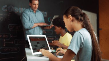 Afrikalı erkek manken tamir ederken beyaz kız programlama ya da kodlama sistemi. Öğretmen elinde dizüstü bilgisayar tutarken çeşitli çocukların web geliştirme programı yazmalarına bakıyor. Yenilik eğitimi. Öğretim.