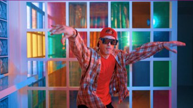 Komik break dansçı kameraya bakarken hiphop 'a doğru serbest adım atıyor. Çılgın mutlu hipster dans edip sokak dansı yaparken Led ışığında günlük kıyafet ve güneş gözlüğü takıyor. Mutluluk.