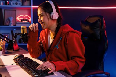 İnternet üzerinden kulaklık takıp gülümseyen Asyalı güzel kız flamasının sunucu kanalı izleyicilerle internet üzerinden konuşma yapıyor. Esport yetenekli takım oyuncuları neon mavi odada. Taktik.
