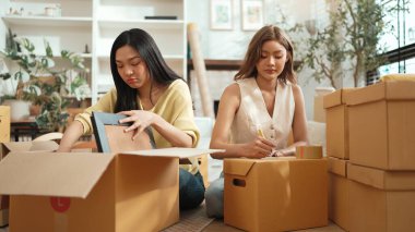 Çekici bir oda arkadaşı oturma odasında paket paketlerken pakette konum yazıyor. Mutlu satıcı birlikte çalışıyor ve teslimat paketini hazırlıyor. Girişimci kargo kutusu paketliyor. Myrmidon.