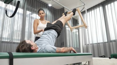 Cadillac ekipmanları üzerinde bacak kaldırma egzersizinde müşteriye yardımcı olan yetenekli pilates eğitmeni. Kadın antrenör, Cadillac 'ın bacak gerdirme hareketine yardım ediyor. Temel bağlantıyı geliştirmek için, bacak esnekliği için. Alışkanlık.