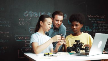 Kafkas öğretmen dizüstü bilgisayara bakarken araba modelleme sistemini kara tahtada kodlama veya programlama koduyla açıklıyor. Robot inşaatını öğrenen çeşitli öğrencileriniz kutlu olsun. Öğretim.