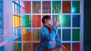 Gece kulübünde kameraya bakarken güneş gözlüklü Asyalı sanatçının serbest dans edişini yakından çek. Mutlu sokak dansçısı dans ediyor ve renkli parlak neon ışıklı ayak izlerini gösteriyor. Mutluluk.