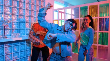 Asyalı adam gece kulübünde çeşitli neon ışıklarda dans ederken kolunu oynatıyor. Modern kulüpte çok kültürlü hippilerle dans eden şık elbiseli mutlu dansçı. Mutluluk.