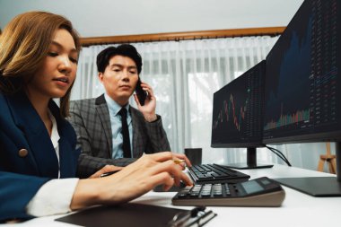 Gülümseyen Asyalı işadamı komisyoncu dinamik borsa veritabanını arıyor. Kadın iş ortağı, iç işyerindeki kar eden uygulama programını karşılaştıran ekranlara işaret ediyor. İnfobahn.