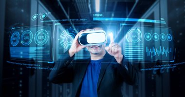 Finansal verileri analiz ederken veri merkezinde duran kulaklıklı bir iş adamı. Yönetici, pazarlama istatistiksel hologramını işaret ediyor ve karar verirken artırılmış gerçeklik gözlükleri kullanıyor. Yaratıcılık.