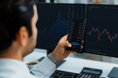 Akıllı telefondan akıllı telefon arayan tüccar işadamı, bilgisayardaki dinamik borsa yatırım ekranını analiz ediyor ve modern merkez ofisteki en kârlı finansal teknoloji pazarına yatırım yapıyor. Tahmin et..