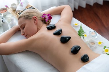 Lüks tatil köyündeki kaplıcalarda sıcak taş masajı. Gün ışığı sükunet ortamında, mutlu kadın müşteri bazalt taş masajından zevk alıyor. Rahatlatıcı bir sıcaklıkla vücudun üzerinde süzülüyor. Sessiz.