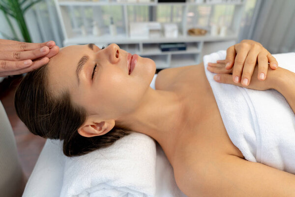 Caucasian woman enjoying relaxing anti-stress head massage and pampering facial beauty skin recreation leisure in dayspa modern light ambient at luxury resort or hotel spa salon. Quiescent