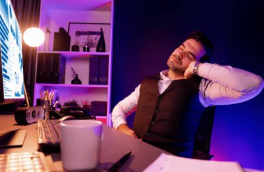 Sırtında, boynunda ve tüm vücudunda ağrıları olan zeki bir iş adamı, esneme hareketleri yapıyor. Gece geç saatlerde mor neon ışıklı odada uzun süre analiz edilen pazar verileri kavramı. Tahmin et..