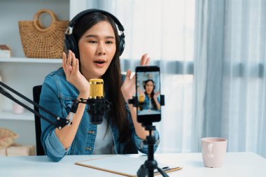 Asyalı sunucu canlı yayında canlı yayında canlı yayında sosyal medyada kulaklık takarak konuşuyor. Dinleyicileri modern stüdyoda koçluk yaparak selamlıyor. Taktik.