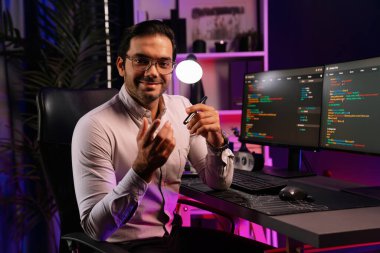 Bilgisayar ekranındaki yazılım geliştirme kodlamasına karşı poz vermek için akıllı bilişim geliştirici görünümlü kamera profilleri, neon ışıklı siber oda ofisinde program güncellemesi internet sitesi verileri sunuyor. Tahmin et..