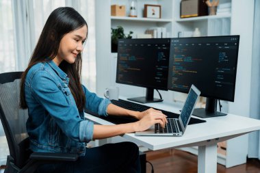 IT geliştiricisinde gülümseyen genç Asyalı dizüstü bilgisayarında kodlama programı verileriyle kotlu tişört giyerek çevrimiçi bilgi yazıyor. Güvenlik analizi iki ekran ile çevrili. Taktik.